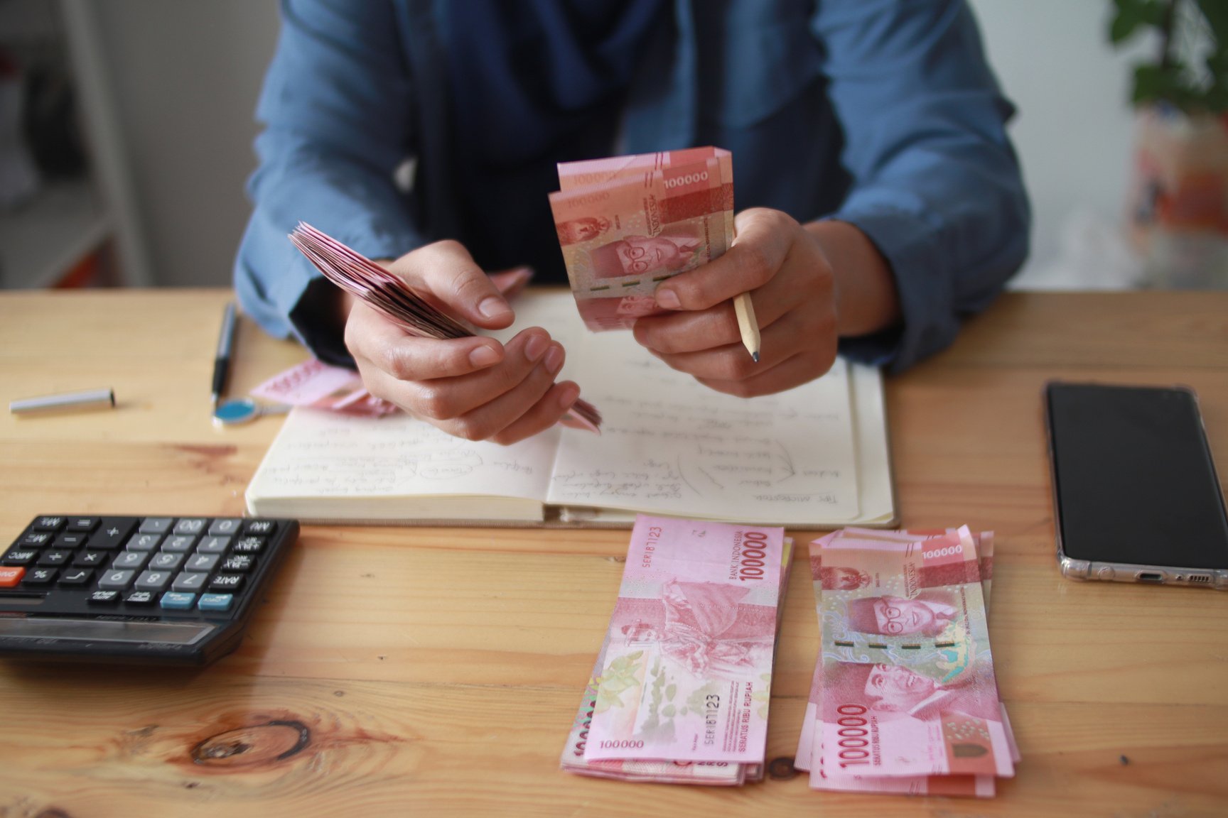 Close up of woman hand counting money uang Indonesian rupiah and making notes, money financial management